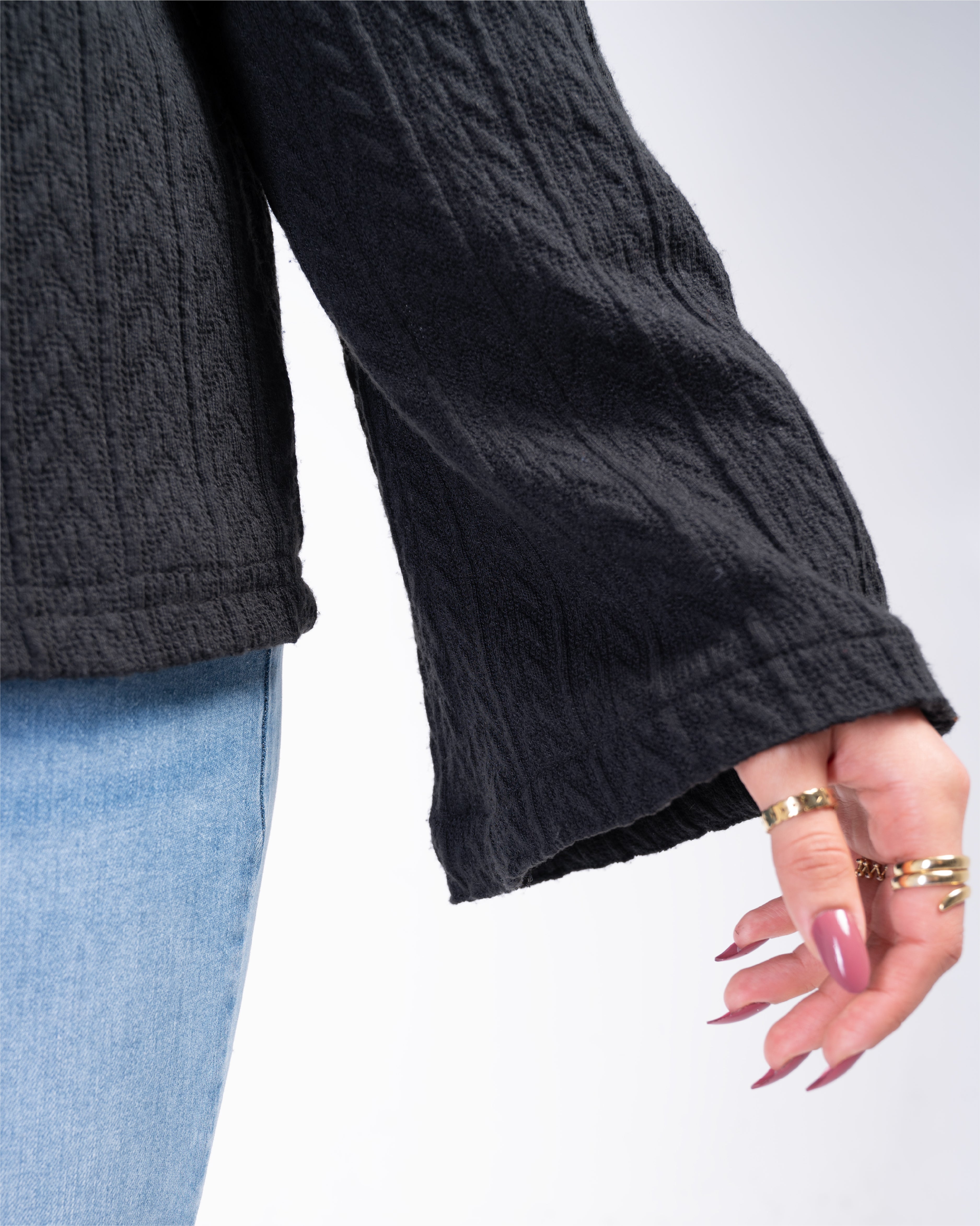 Close-up of a person wearing a dark gray cable knit sweater with light blue jeans on a white background.