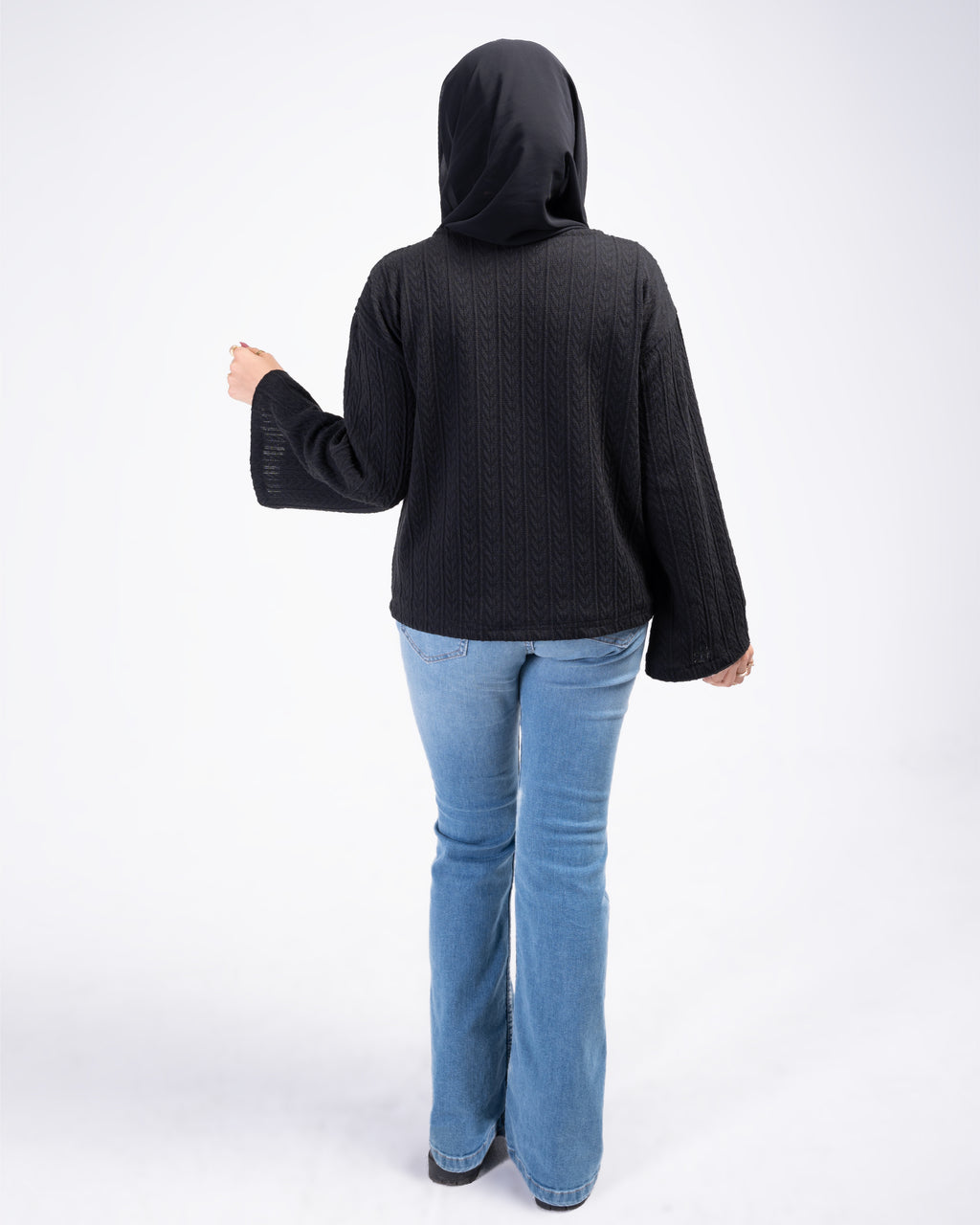 Person wearing a black knit cardigan and light blue jeans on a white background