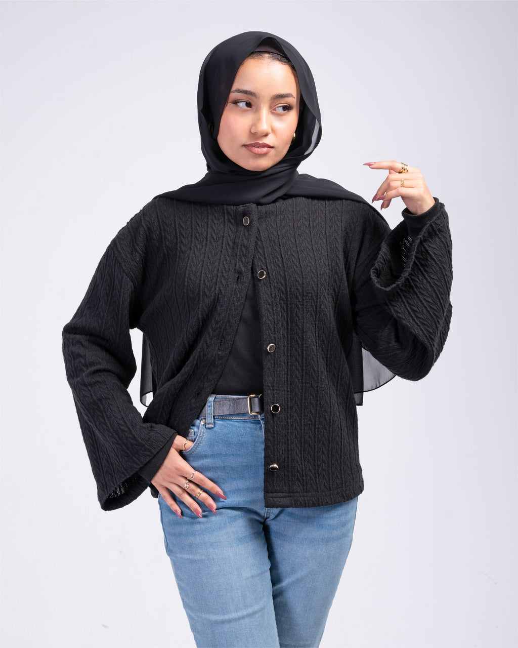 Woman wearing a black cardigan over a black top with blue jeans on a white background