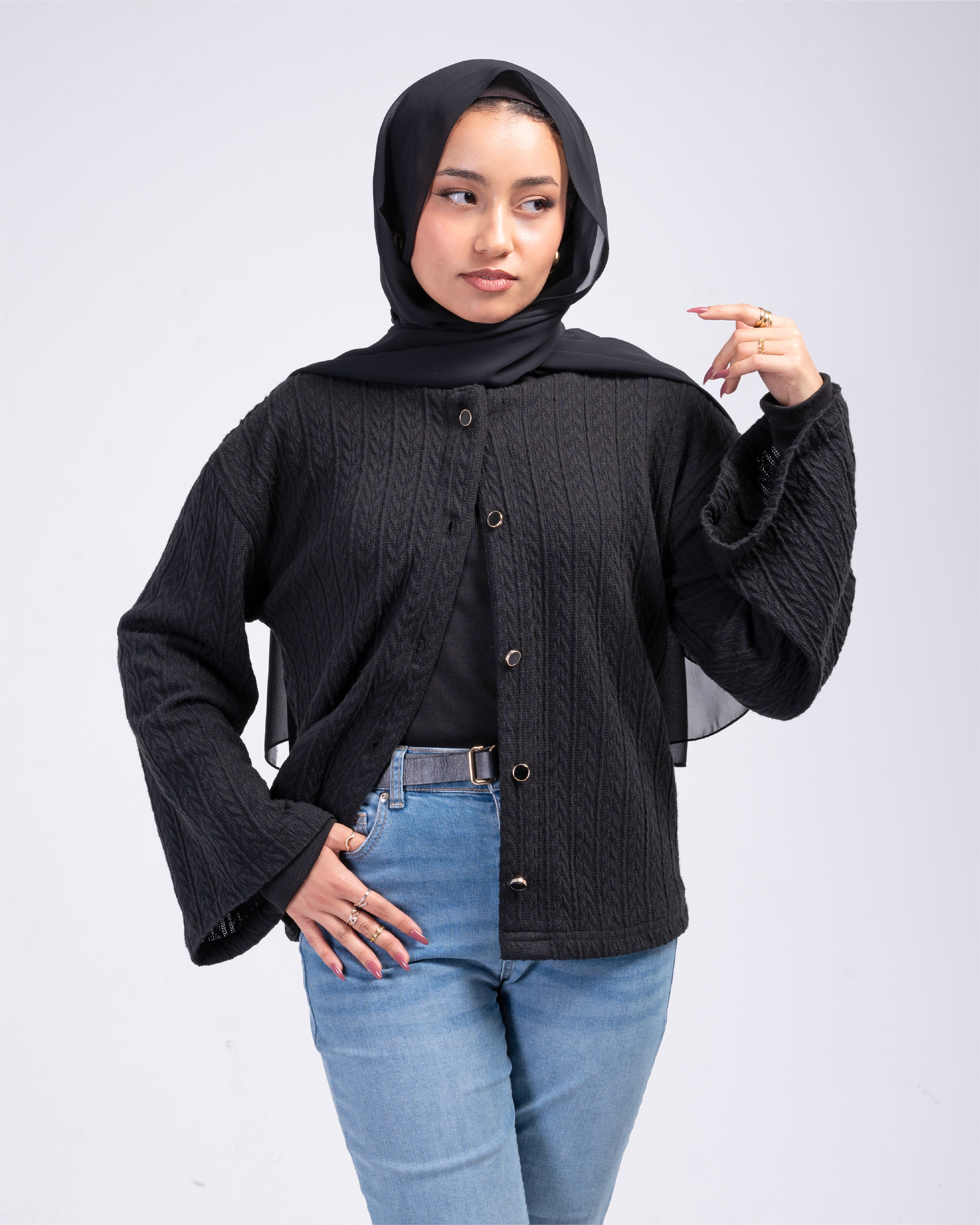 Woman wearing a black cardigan over a black top with blue jeans on a white background