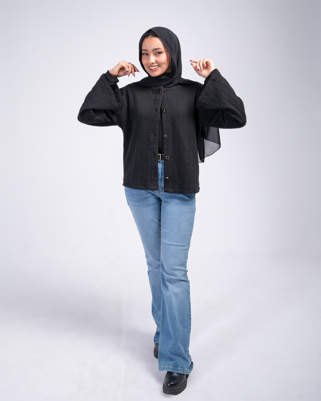 Woman wearing a black cardigan and blue jeans on a white background