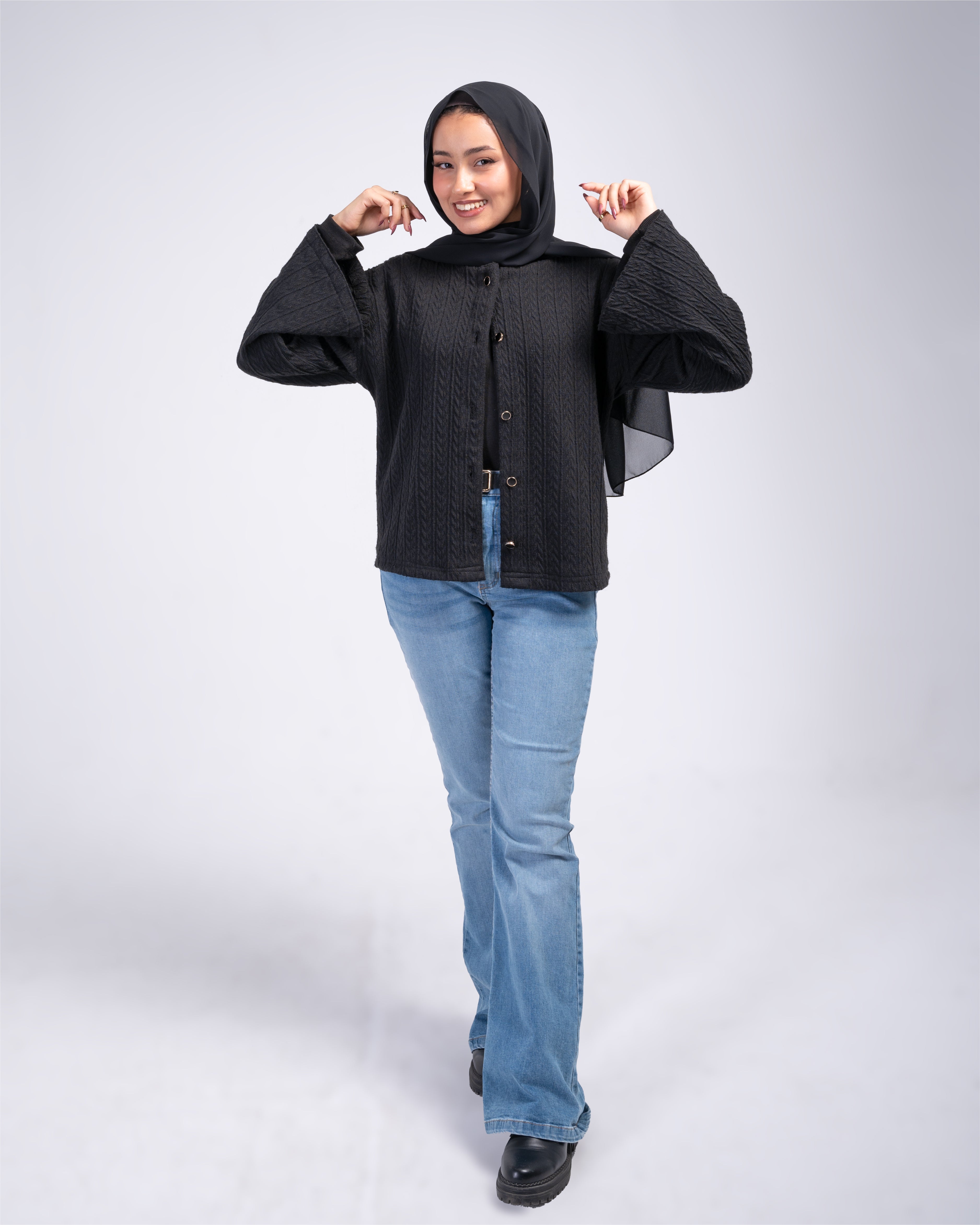 Woman wearing a black cardigan and blue jeans on a white background